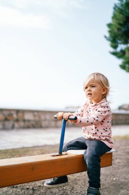 Küçük kız salıncak dengeleyicisine oturur ve kolu tutar. Yüksek kalite fotoğraf