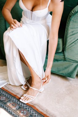 Gelin, sandalyede otururken yüksek topuklu ayakkabılarını bağlar. Kırpılmış. Yüzsüz. Yüksek kalite fotoğraf