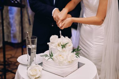 Gelin ve damat masada bir bıçakla düğün pastası kestiler. Kırpılmış. Yüzsüz. Yüksek kalite fotoğraf