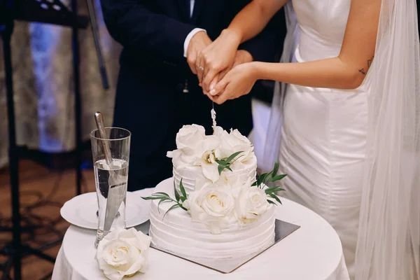 Bride and groom cut a wedding cake with a knife on a table. Cropped. Faceless. High quality photo