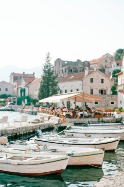 Kıyıya yakın bir yerde balıkçı tekneleri antik evlerin yakınlarındaki bir gölgeliğin altında bir restoranla demirlemişti. Perast, Karadağ. Yüksek kalite fotoğraf