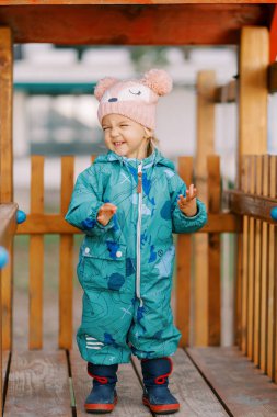 Parktaki çitin yanındaki ahşap platformda gülümseyen küçük kız. Yüksek kalite fotoğraf