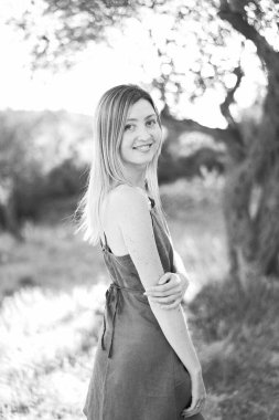 Gülümseyen kız parkta yarım yamalak duruyor, eliyle dirseğine dokunuyor. Siyah beyaz fotoğraf. Yüksek kalite fotoğraf