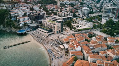Budva 'nın eski ve yeni kısımları arasında deniz kıyısında güneş şemsiyeleri olan plaj. Karadağ. Drone. Yüksek kalite fotoğraf