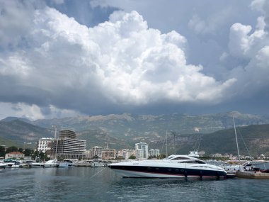 Yat, kıyıdaki yüksek binalarla rıhtıma demirlemiş beyaz bulutlar içindeki dağların arka planına karşı. Yüksek kalite fotoğraf