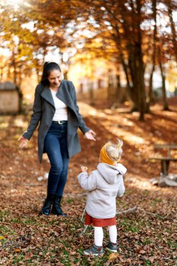 Gülümseyen anne, sonbahar ormanında küçük bir kıza doğru yürüyor. Yüksek kalite fotoğraf