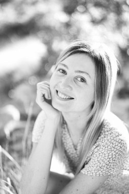 Gülümseyen genç kadın çimenlerde oturuyor, başını elinin üzerine koyuyor. Siyah beyaz fotoğraf. Yüksek kalite fotoğraf