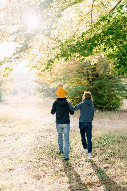 Annem, sonbahar parkında yürürken babama kucağında küçük bir çocuk taşırken sarıldı. Arkadan bak. Yüksek kalite fotoğraf
