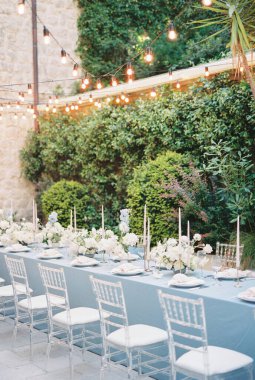 Yeşil çalıların yakınında ampul çelenkleri olan eski bir evin avlusunda uzun bir şenlik masası duruyor. Yüksek kalite fotoğraf