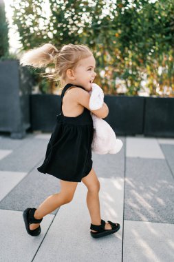 Uçan saçlı küçük bir kız bahçede oyuncak bir tavşana sarılıyor. Yüksek kalite fotoğraf