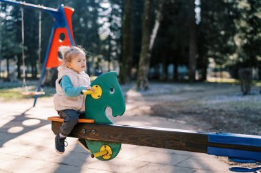 Küçük kız parkta salıncak dengeleyicisine oturuyor. Yan görüş. Yüksek kalite fotoğraf