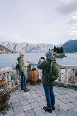 Adam, deniz kenarındaki bir korkuluğa yaslanmış bir kadının fotoğrafını çekiyor. Arkadan bak. Yüksek kalite fotoğraf