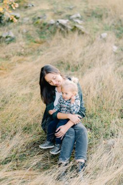 Gülümseyen anne, parkta çimlerin üzerinde oturan küçük kızına bakıyor. Yüksek kalite fotoğraf