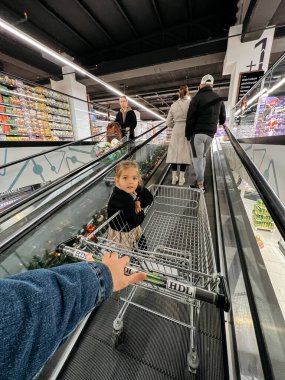 Babam ve küçük bir kız alışveriş merkezinde bir alışveriş arabasıyla yürüyen merdivene biniyor. Yüksek kalite fotoğraf