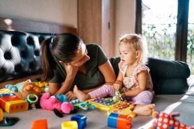 Annem küçük kızına bakar ve yanında uzanan oyuncaklarla oynar. Yüksek kalite fotoğraf
