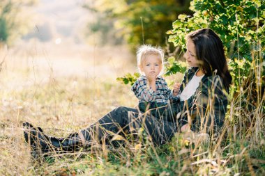Annem çimenlerde oturur ve kucağında oturan küçük kıza bakar. Yüksek kalite fotoğraf
