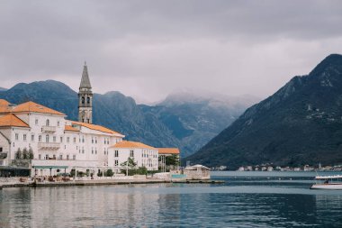 Aziz Niklas Kilisesi 'nin çan kulesi Perast evlerinin kırmızı kiremitli çatılarının üzerinde sisli dağların arka planına karşı. Karadağ. Yüksek kalite fotoğraf