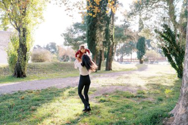 Annem sonbahar parkında kucağına küçük bir kız atar. Arkadan bak. Yüksek kalite fotoğraf