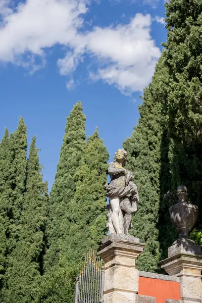 Ancient statue of a woman stands on a pedestal at the gate in the green garden of the villa. High quality photo