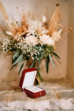 Alyanslar gelin buketinin yanındaki kutuda taş bir duvarın içinde duruyor. Yüksek kalite fotoğraf