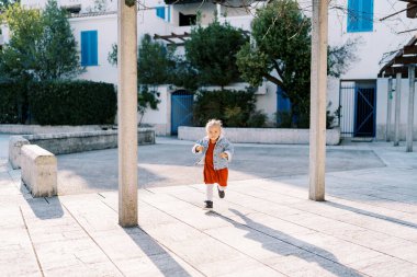 Küçük kız sütunlar arasındaki üç katlı evin yanındaki fayanslı avluda koşuyor. Yüksek kalite fotoğraf