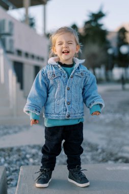 Küçük gülen kız binanın yakınındaki beton bir çitin üzerinde duruyor. Yüksek kalite fotoğraf