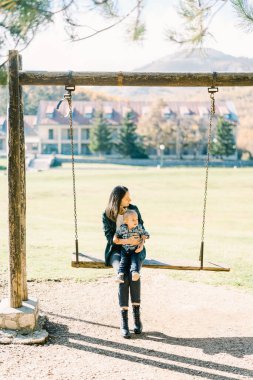 Küçük kız parktaki büyük bir salıncakta annesinin kucağında oturuyor. Yüksek kalite fotoğraf