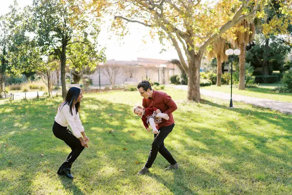 Babası kucağında küçük bir kızla parkta gülen bir anneye koşuyor. Yüksek kalite fotoğraf