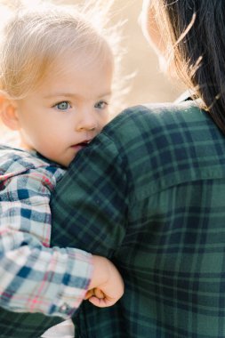Küçük kız çenesi omzunda annesinin kollarında oturuyor. Arkadan bak. Kırpılmış. Yüksek kalite fotoğraf
