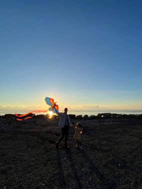 Anne ve küçük bir kız elinde uçurtmayla gün batımının arka planında duruyorlar. Yüksek kalite fotoğraf