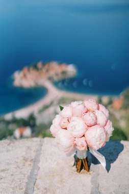 Düğün buketi denizin üstündeki bir dağda taş bir çitin üzerinde duruyor. Yüksek kalite fotoğraf