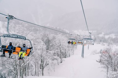 Kayakçılar dağdaki karlı bir ormanın üzerinde dört koltuklu asansöre biniyorlar. Yüksek kalite fotoğraf