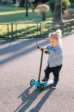 Küçük kız yolda scooterıyla durup düşünüyor. Yüksek kalite fotoğraf