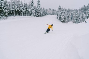 Sarı bir kayak takımı giymiş snowboardcu, karlı bir dağın yamacına yaslanmış bir snowboard 'a biniyor. Yüksek kalite fotoğraf