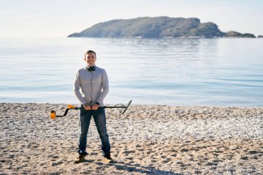 Kumsalda elinde metal detektörle duran gülümseyen genç adam. Yüksek kalite fotoğraf