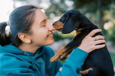 Siyah köpek yavrusu, onu kollarında tutan gülümseyen bir kızın burnunu yalıyor. Yüksek kalite fotoğraf