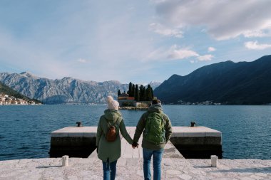 Erkek ve kadın St. George Adası 'na bakan bir rıhtımda el ele yürüyorlar. Karadağ. Arkadan bak. Yüksek kalite fotoğraf