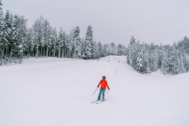 Kırmızı bir kayak kıyafeti giyen kayakçı, karlı bir yamaçtan aşağı iniyor ve direklerini yana çeviriyor. Yüksek kalite fotoğraf