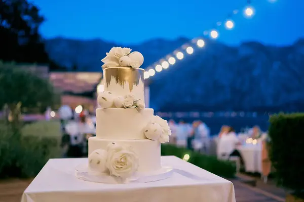 Three-tier wedding cake stands on a table in an evening garden with illumination. High quality photo