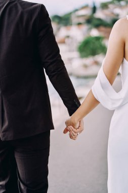 Gelin ve damat yolda el ele tutuşuyorlar. Arkadan bak. Kırpılmış. Yüksek kalite fotoğraf