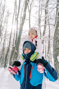 Babası omuzlarında küçük bir kızla karlı bir ormanda yürüyor. Yüksek kalite fotoğraf