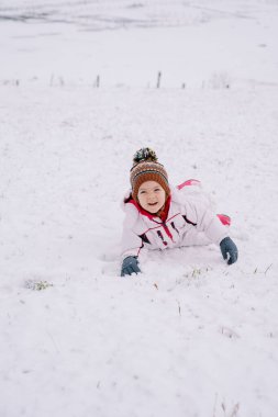 Karda yüzüstü yatan gülümseyen küçük kız. Yüksek kalite fotoğraf