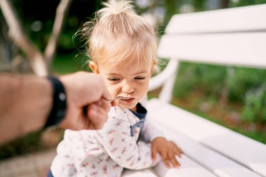 Babam, parktaki bankta duran küçük bir kıza kaşıktan yulaf lapası veriyor. Yüksek kalite fotoğraf