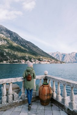 Kadın kıyıda duruyor, bir korkuluğa yaslanıyor ve dağlara bakıyor. Arkadan bak. Yüksek kalite fotoğraf