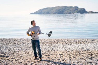 Sahilde metal dedektörlü bir plaj polisi bekliyor. Yüksek kalite fotoğraf