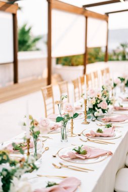 Çiçek buketleri uzun bir şenlik masasının üzerinde, mumların yanında ve tabakta küçük narlar. Yüksek kalite fotoğraf
