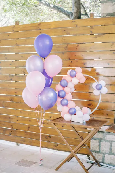 Round decor of colorful inflatable balloons stands on a table near a wooden fence. High quality photo