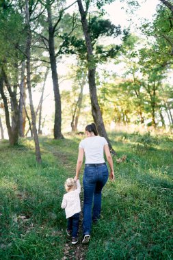 Anne ve küçük bir kız ormanda el ele tutuşarak bir patika boyunca yürüyorlar. Arkadan bak. Yüksek kalite fotoğraf