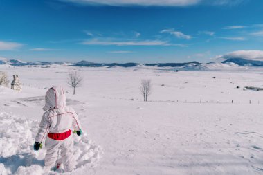 Küçük kız bir vadide derin bir kar yığınında duruyor ve dağlara bakıyor. Arkadan bak. Yüksek kalite fotoğraf