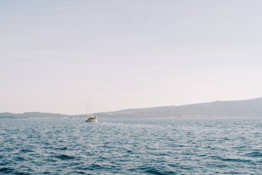 Mavi bir körfez boyunca uzanan yat, açık bir sis bulutuyla bir dağ sırasının arka planına doğru ilerliyor. Yüksek kalite fotoğraf